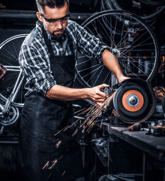 Skilled repairmaster is working with machine tool at busy bucycle workshop.